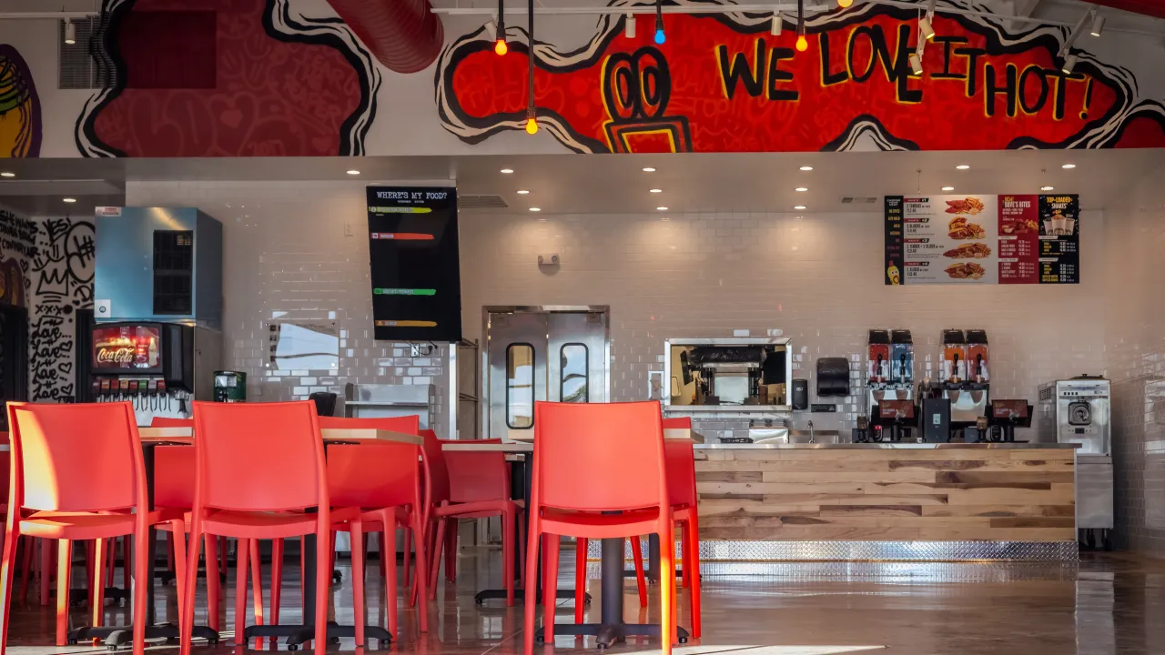 Interior view of Dave's Hot Chicken on E. Oak St, Conway, AR, featuring vibrant red chairs and colorful wall murals.