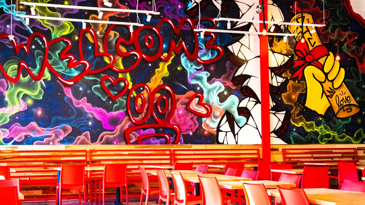 Interior view of Dave's Hot Chicken on E. Oak St, Conway, AR, showcasing vibrant murals and colorful red seating.