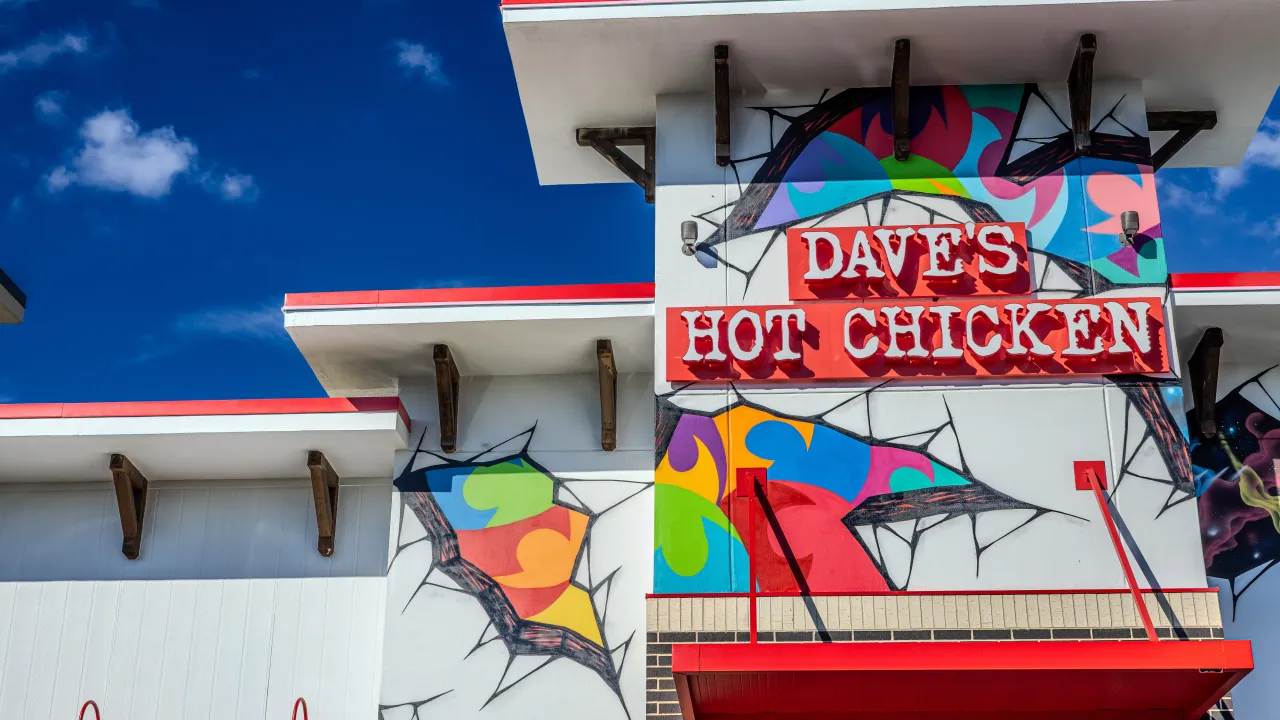 Exterior view of Dave's Hot Chicken at 1120 E. Oak St., Conway, AR, showcasing vibrant murals and bold red signage.