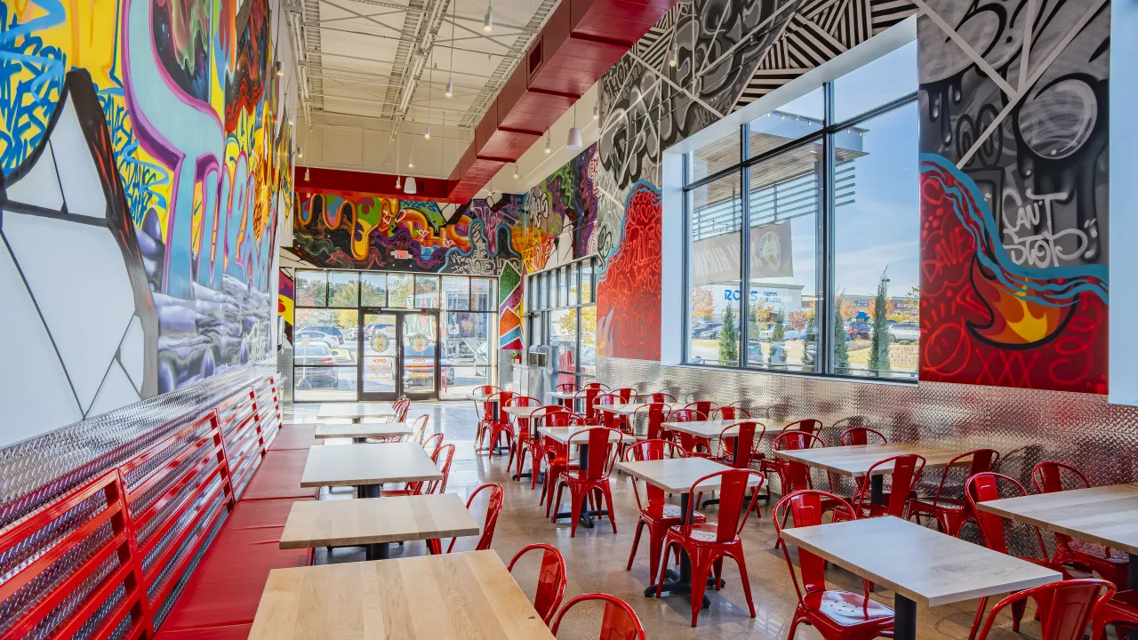 Interior view of Dave's Hot Chicken on S. Olympia Avenue, Tulsa, OK, showcasing colorful murals and modern red seating.