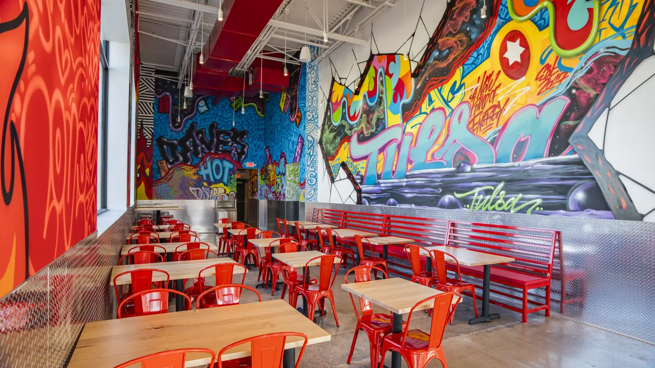 Interior view of Dave's Hot Chicken on S. Olympia Avenue, Tulsa, OK, showcasing vibrant murals and red seating.