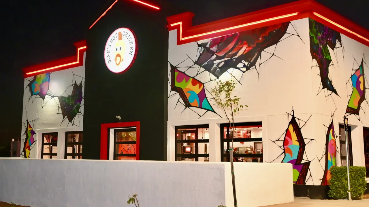 Exterior view of Dave's Hot Chicken on E. Shaw Avenue, Fresno, CA, showcasing vibrant murals and red neon lighting.