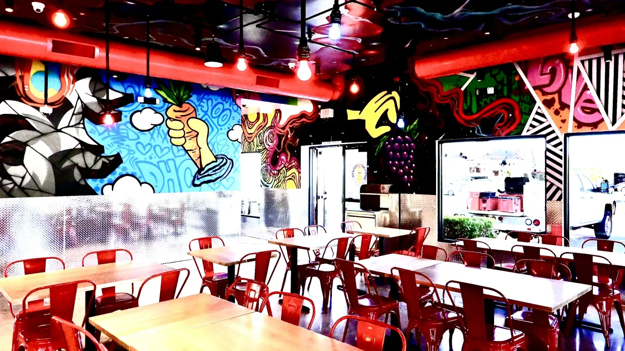 Interior view of Dave's Hot Chicken on E. Shaw Avenue, Fresno, CA, showcasing vibrant murals and red metal seating.