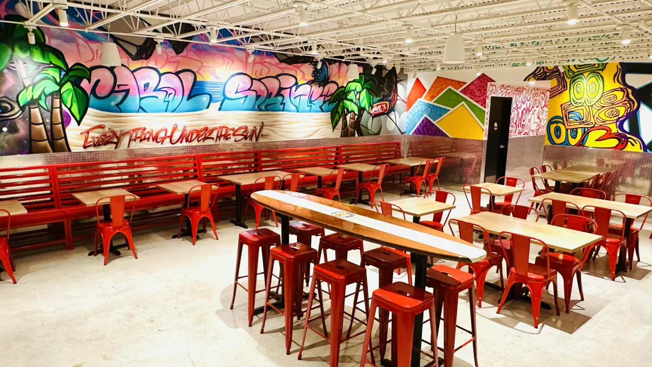 Interior view of Dave's Hot Chicken on N. University Dr, Coral Springs, FL, featuring vibrant murals and red seating.