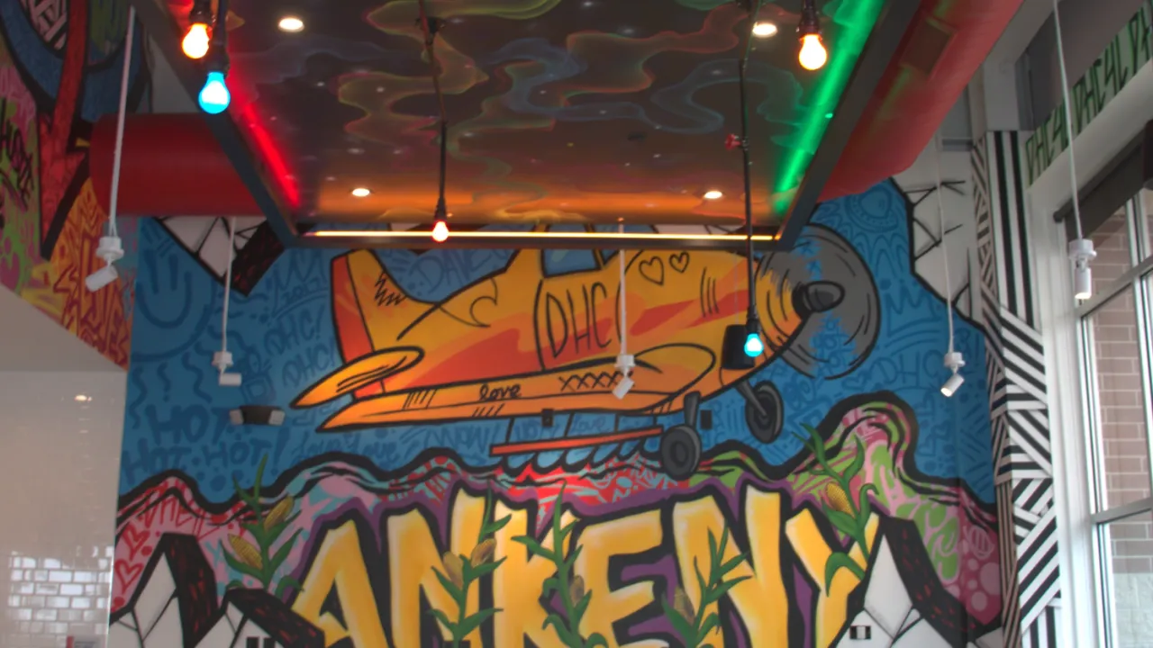 Interior view of Dave's Hot Chicken in Ankeny, IA, showcasing vibrant murals and colorful hanging lights.