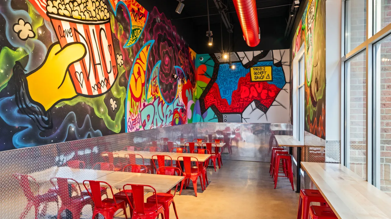 Interior view of Dave's Hot Chicken on N. Fairfield Road, Beavercreek, OH, showcasing vibrant murals and red metal seating.