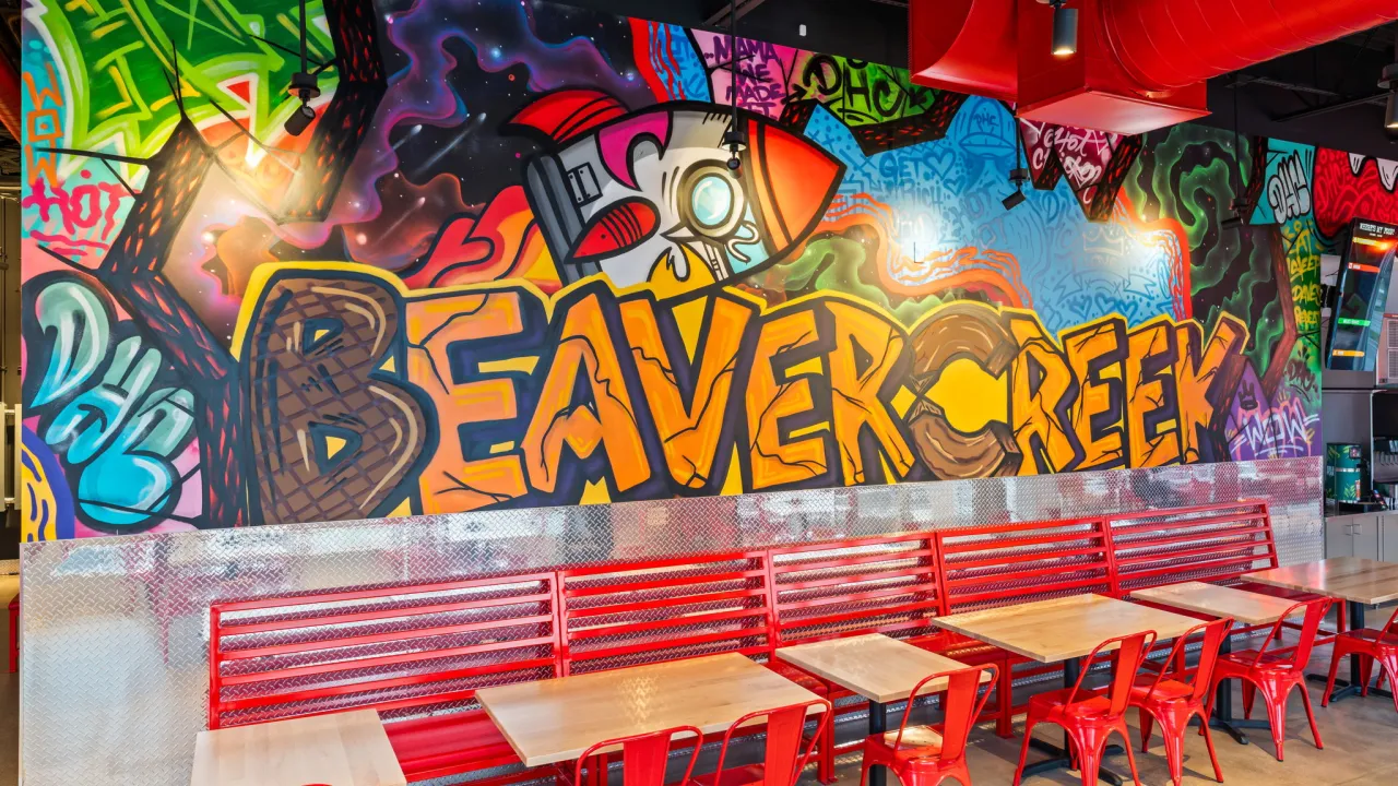 Interior view of Dave's Hot Chicken at 2650 N. Fairfield Road, Beavercreek, OH, showcasing vibrant graffiti and red seating.