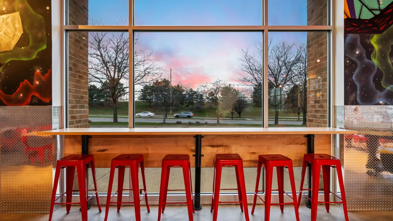Interior view of Dave's Hot Chicken on Fairfield Road, Beavercreek, OH, featuring red stools and colorful wall art.