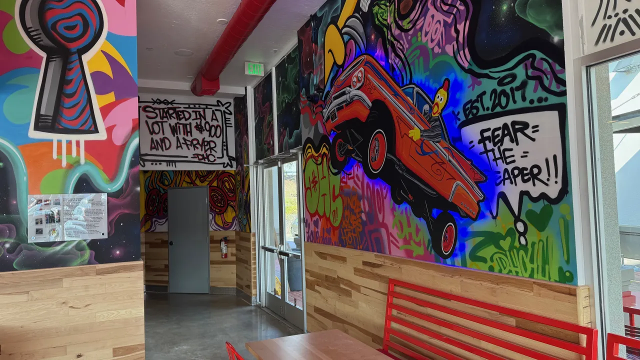 Interior view of Dave's Hot Chicken at 2714 Pinole Valley Rd, Pinole, CA, showcasing vibrant murals and red furniture.