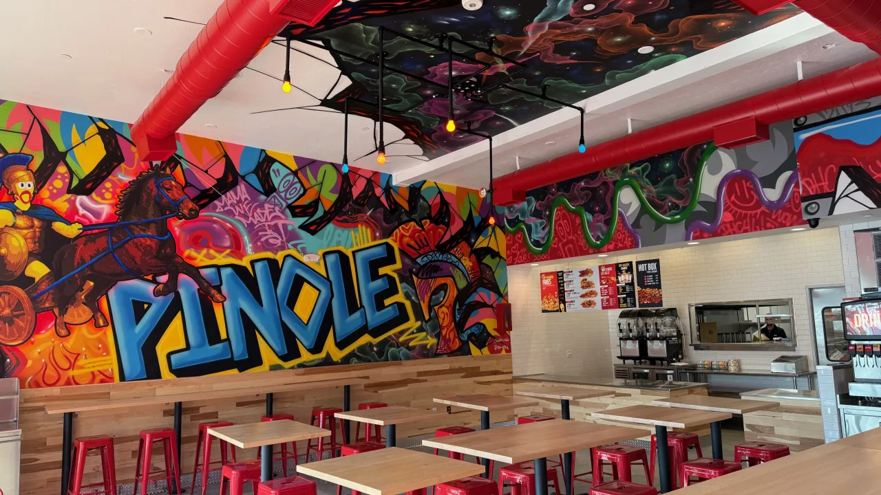 Interior view of Dave's Hot Chicken at 2714 Pinole Valley Rd, Pinole, CA, showcasing vibrant murals and red stools.