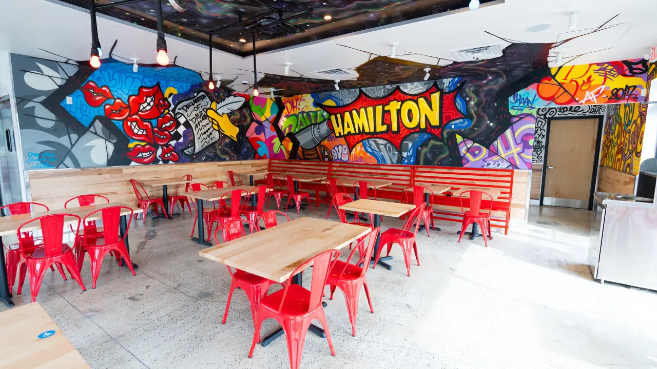 Interior view of Dave's Hot Chicken on Route 33, Hamilton, NJ, showcasing vibrant murals and red metal chairs.