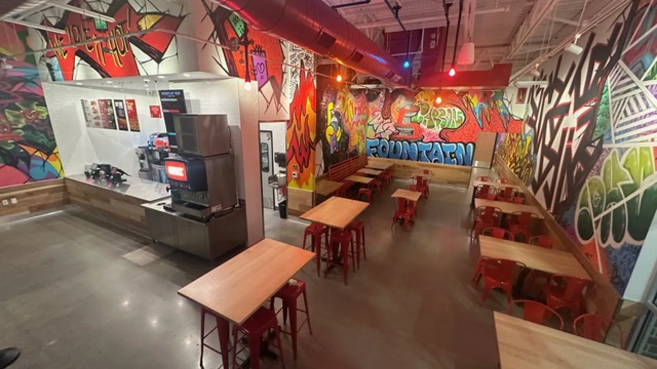Interior view of Dave's Hot Chicken in Fountain, CO, showcasing vibrant murals, red seating, and a modern counter area.