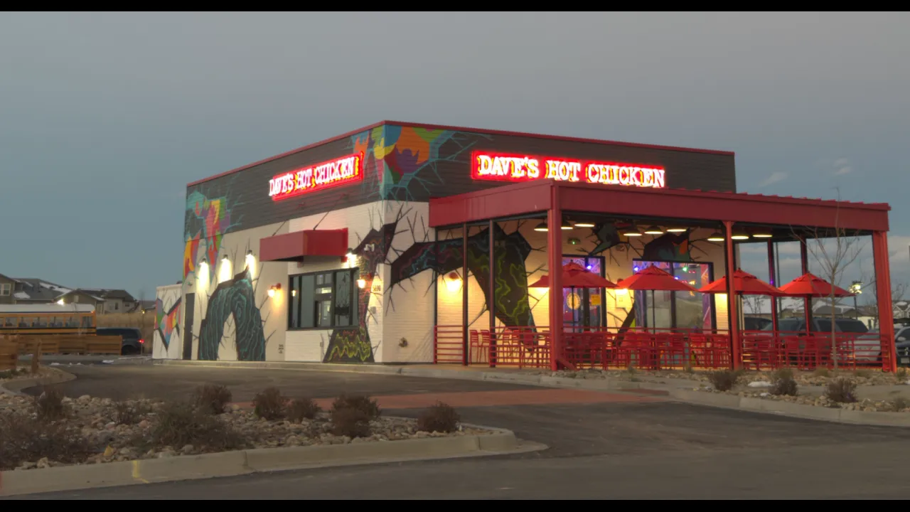 Exterior view of Dave's Hot Chicken on Tower Rd, Denver, CO, showcasing vibrant murals and outdoor red seating.