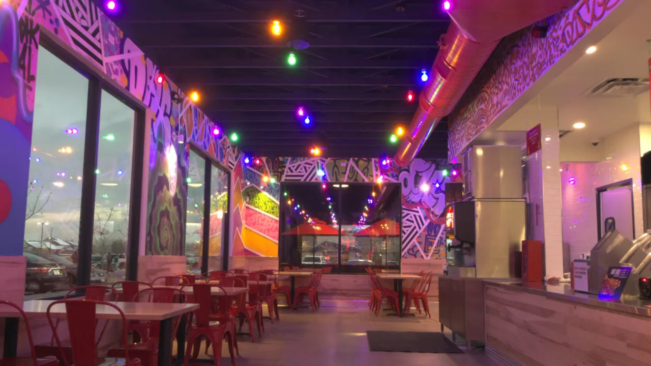 Interior view of Dave's Hot Chicken on Tower Rd, Denver, CO, showcasing vibrant murals and colorful lighting.
