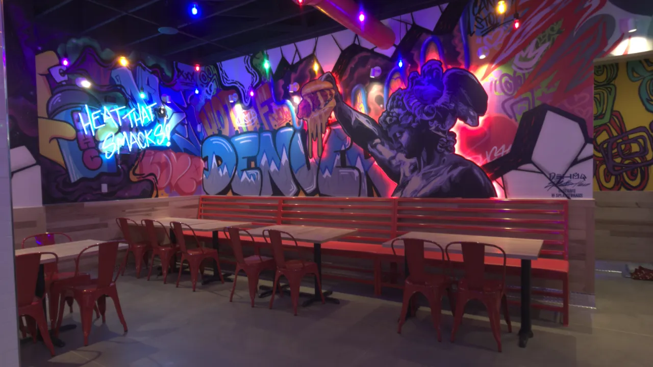 Interior view of Dave's Hot Chicken on Tower Rd, Denver, CO, showcasing vibrant murals and red metal furniture.