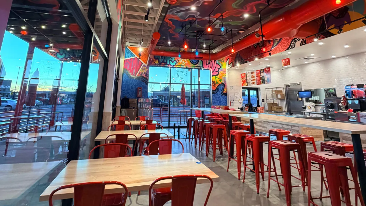 Interior view of Dave's Hot Chicken on Iola Street, Aurora, CO, featuring vibrant mural, red stools, and modern decor.