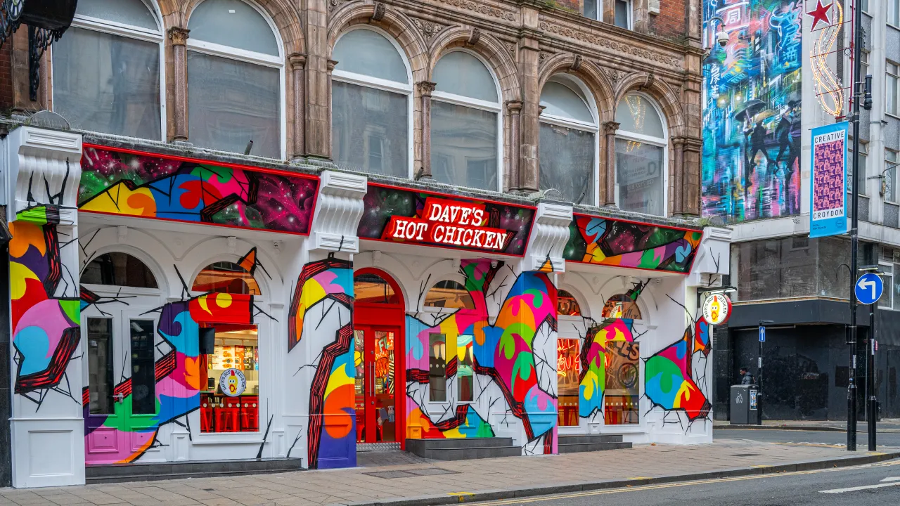 Exterior view of Dave's Hot Chicken on High St, Croydon, featuring vibrant murals and bold red signage.