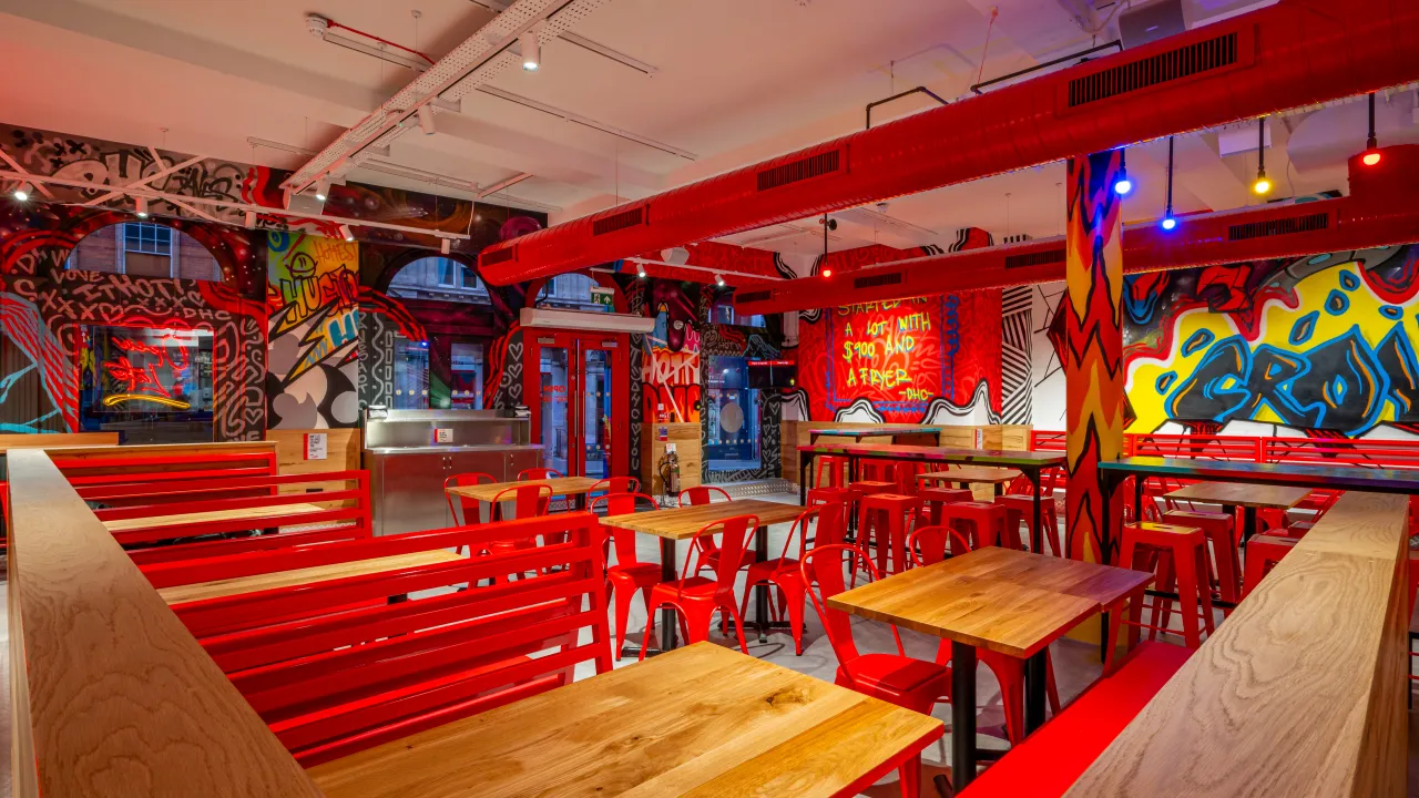 Interior view of Dave's Hot Chicken on High St, Croydon, featuring vibrant murals, red furniture, and a lively atmosphere.
