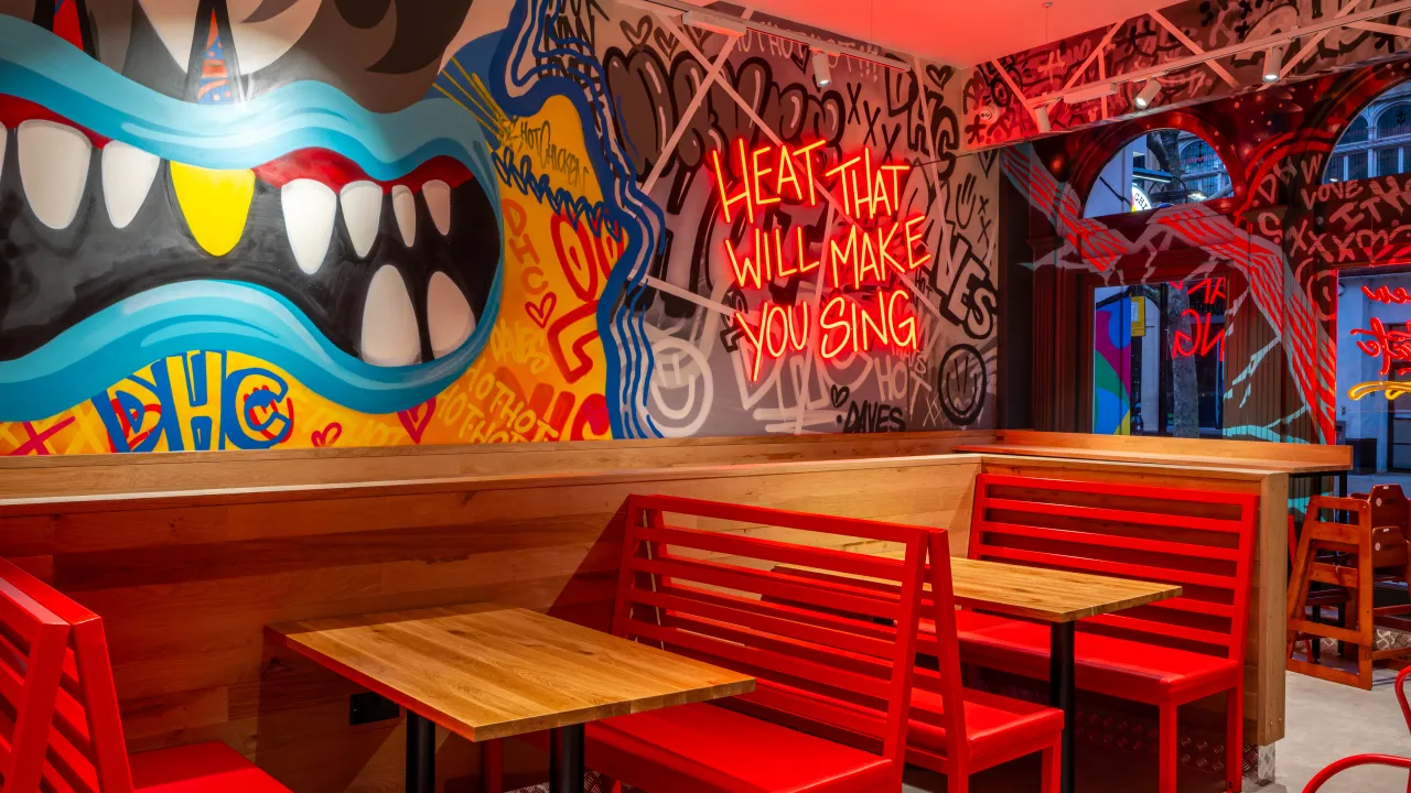 Interior view of Dave's Hot Chicken at 7/11 High St, Croydon, featuring vibrant murals and red seating.