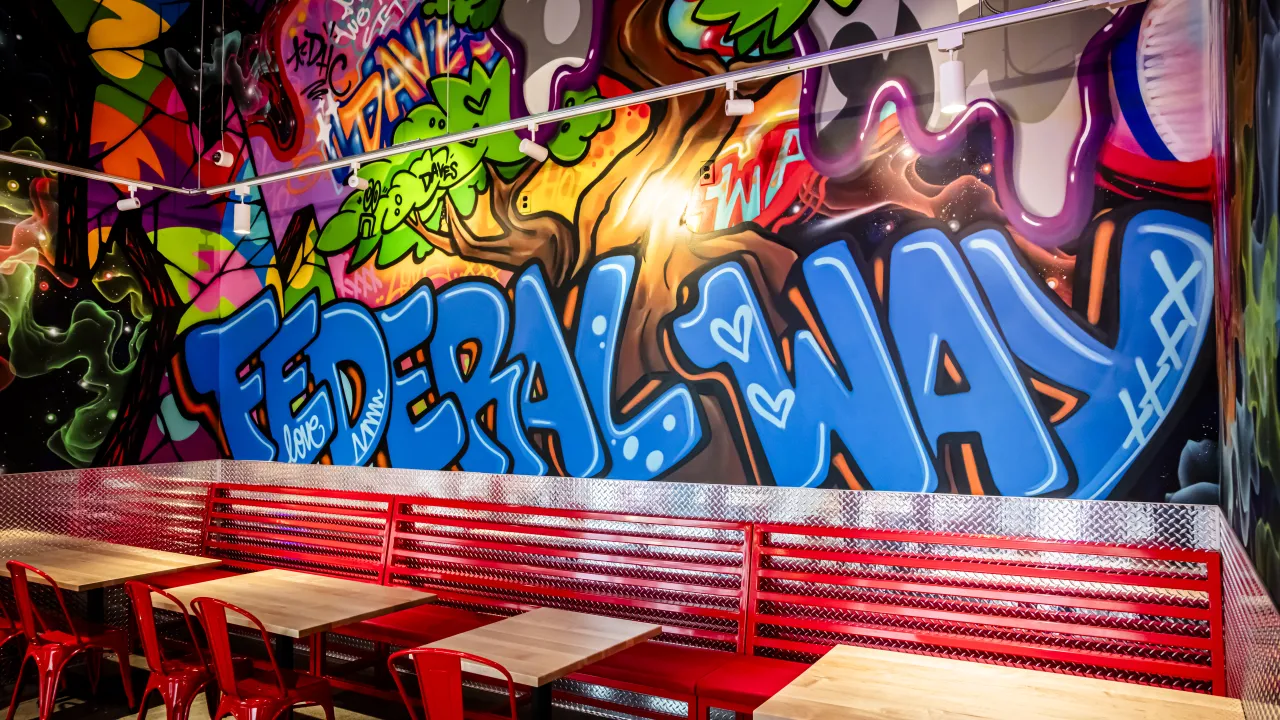 Interior shot of Dave's Hot Chicken at 1701 S Commons, Federal Way, WA, featuring vibrant graffiti and red seating.