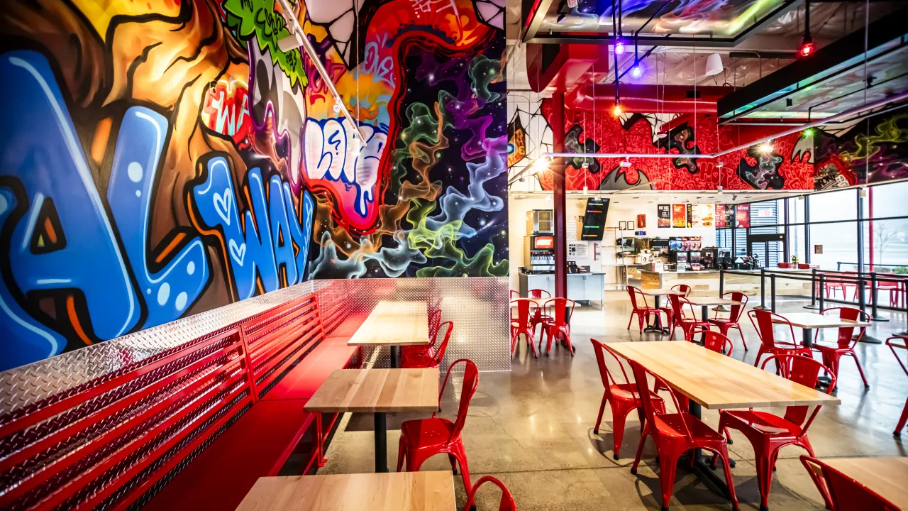 Interior view of Dave's Hot Chicken at 1701 S Commons, Federal Way, WA, showcasing vibrant murals and red seating.