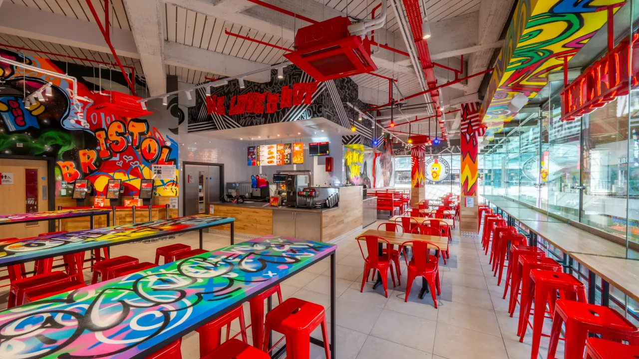 Interior view of a vibrant restaurant in Bristol, featuring colorful graffiti, red chairs, and a welcoming counter area.