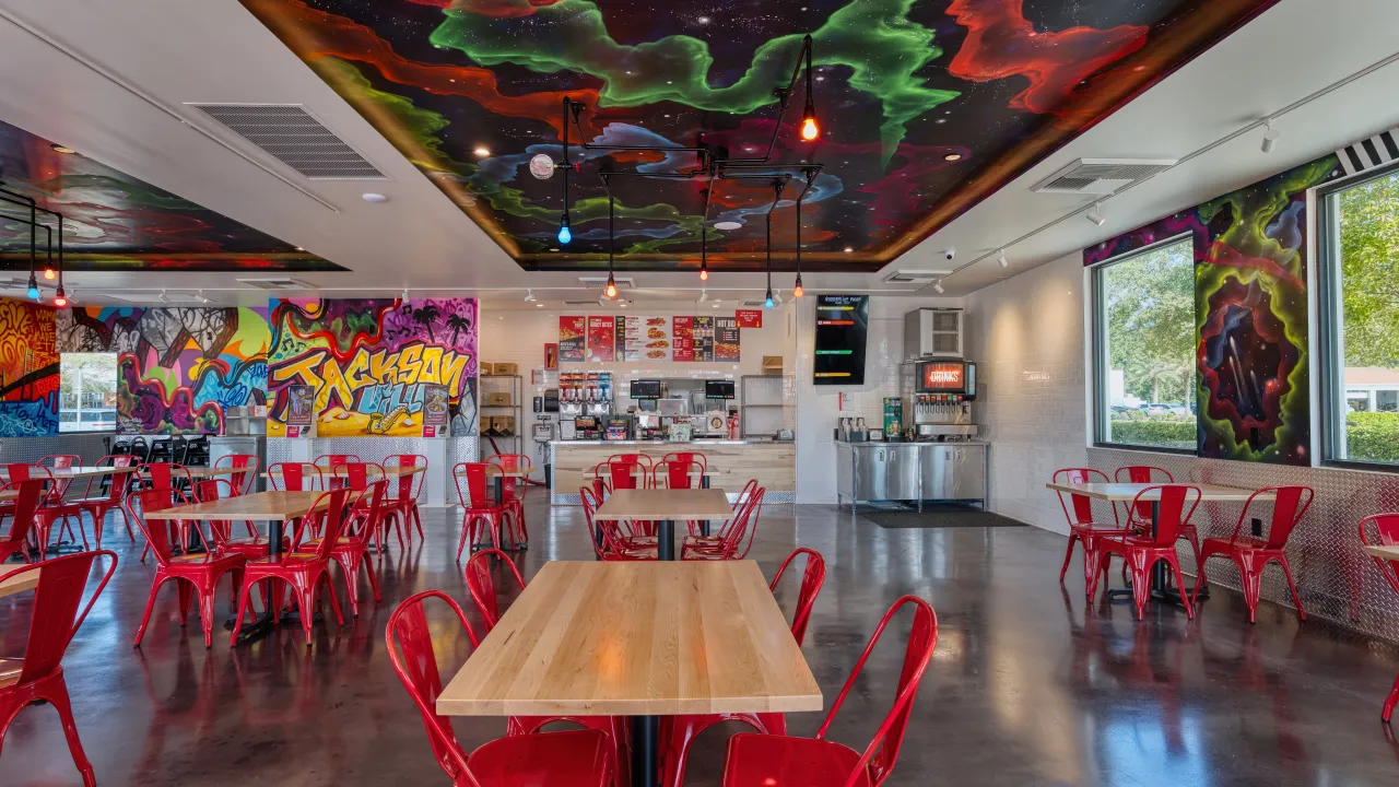 Interior view of Dave’s Hot Chicken on Skymarks Drive, Jacksonville, FL, featuring vibrant murals and red metal chairs.