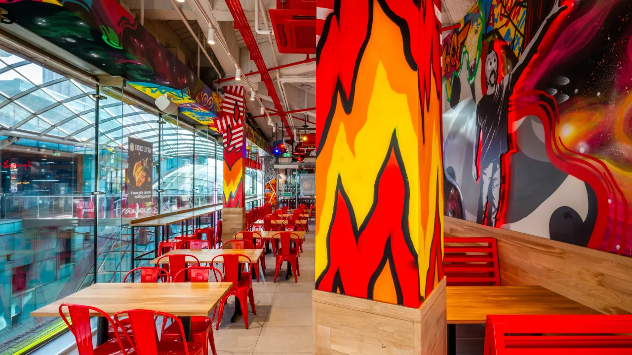 Interior view of a vibrant restaurant, showcasing colorful murals and red furniture in a lively atmosphere.