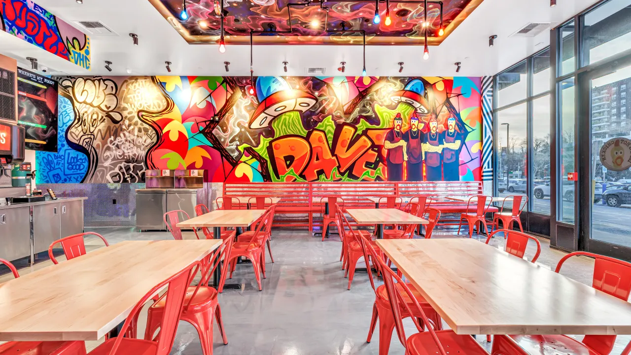 Interior view of Dave’s Hot Chicken on 56th Ave, Laveen, AZ, featuring vibrant murals and red metal seating.