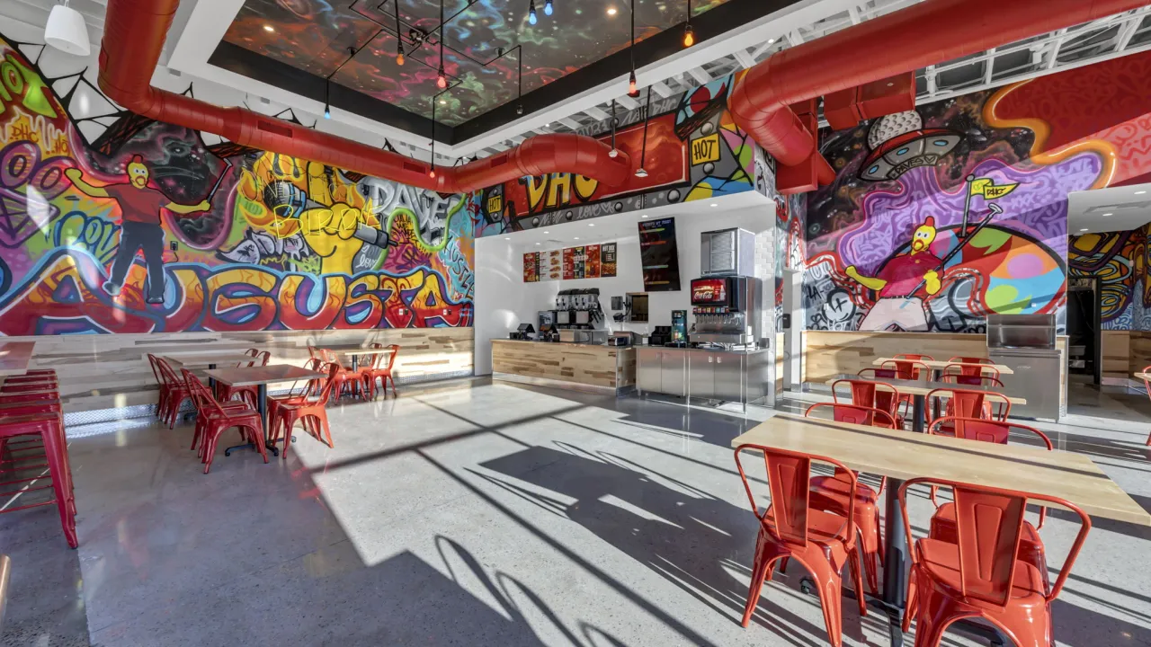 Interior view of vibrant restaurant at 1102 Trust Ave, Augusta, GA, showcasing colorful murals and red metal chairs.