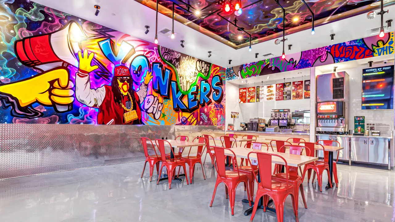 Interior view of a vibrant dining area at Dave’s Hot Chicken, featuring colorful murals and red metal chairs in Laveen, AZ.