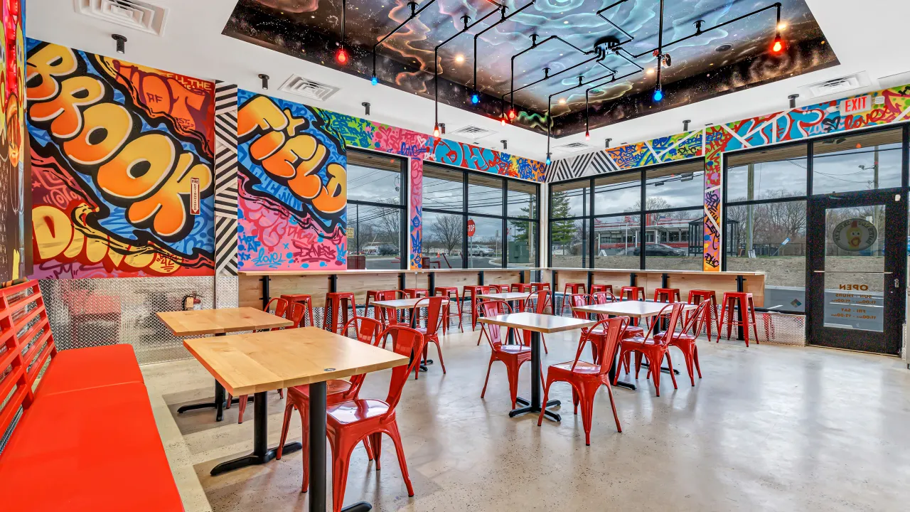Interior view of Dave’s Hot Chicken on Federal Rd, Brookfield, CT, showcasing vibrant murals and red chairs.