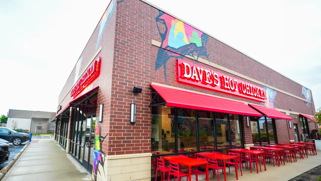 Exterior view of Dave's Hot Chicken at 5530 W. Touhy Ave, Skokie, IL, showcasing vibrant murals and red patio furniture.