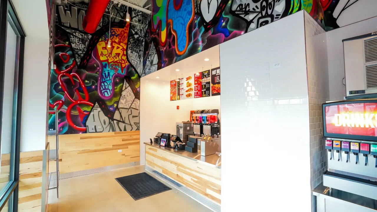 Interior view of vibrant eatery at 5530 W. Touhy Ave, Skokie, IL, showcasing colorful graffiti wall and modern counter.
